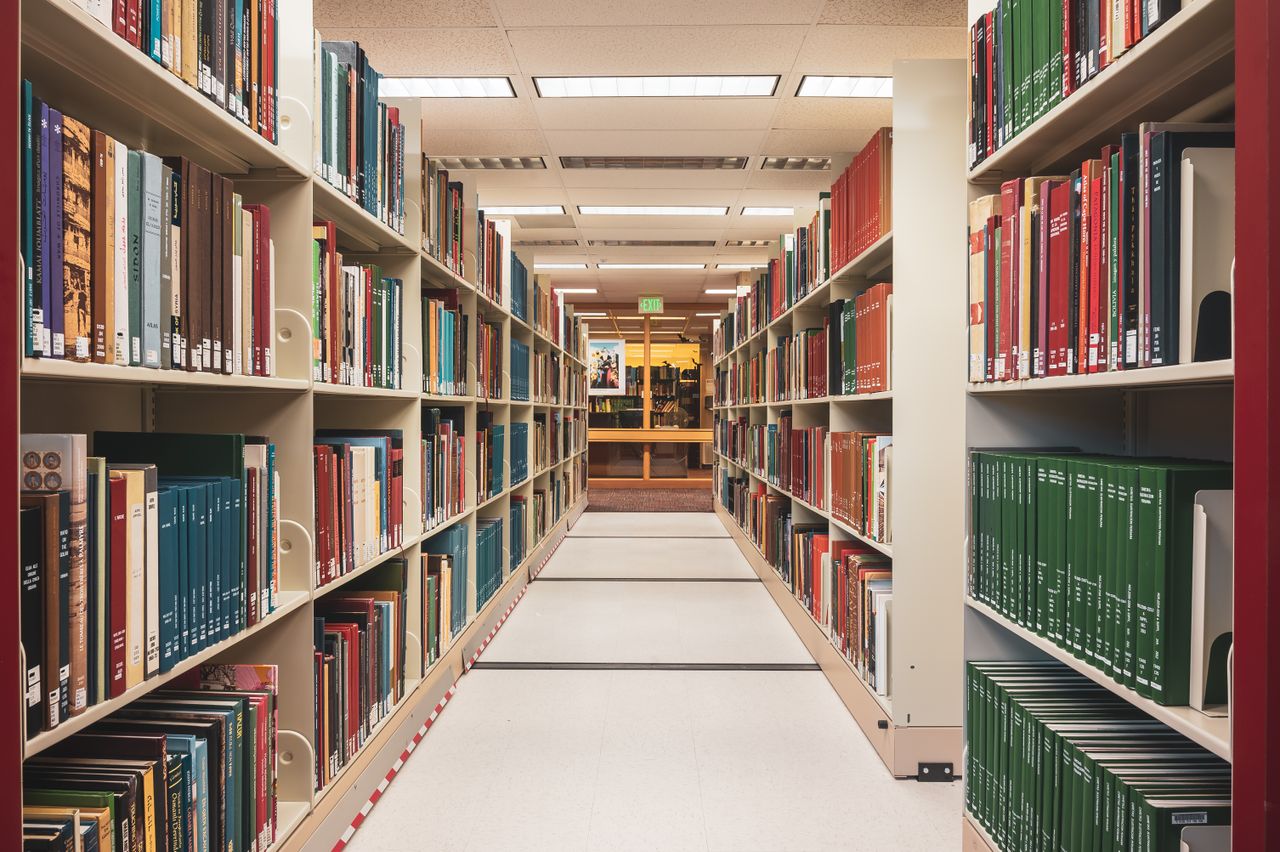 Services Long aisle in a library with shelves full of various colorful books, perfect for education and research.