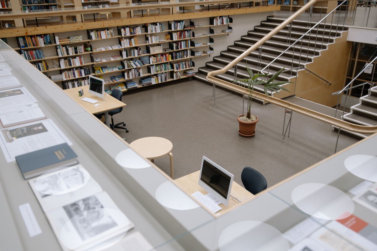 Home Spacious university library interior featuring bookshelves, desks, and a staircase for study and research.