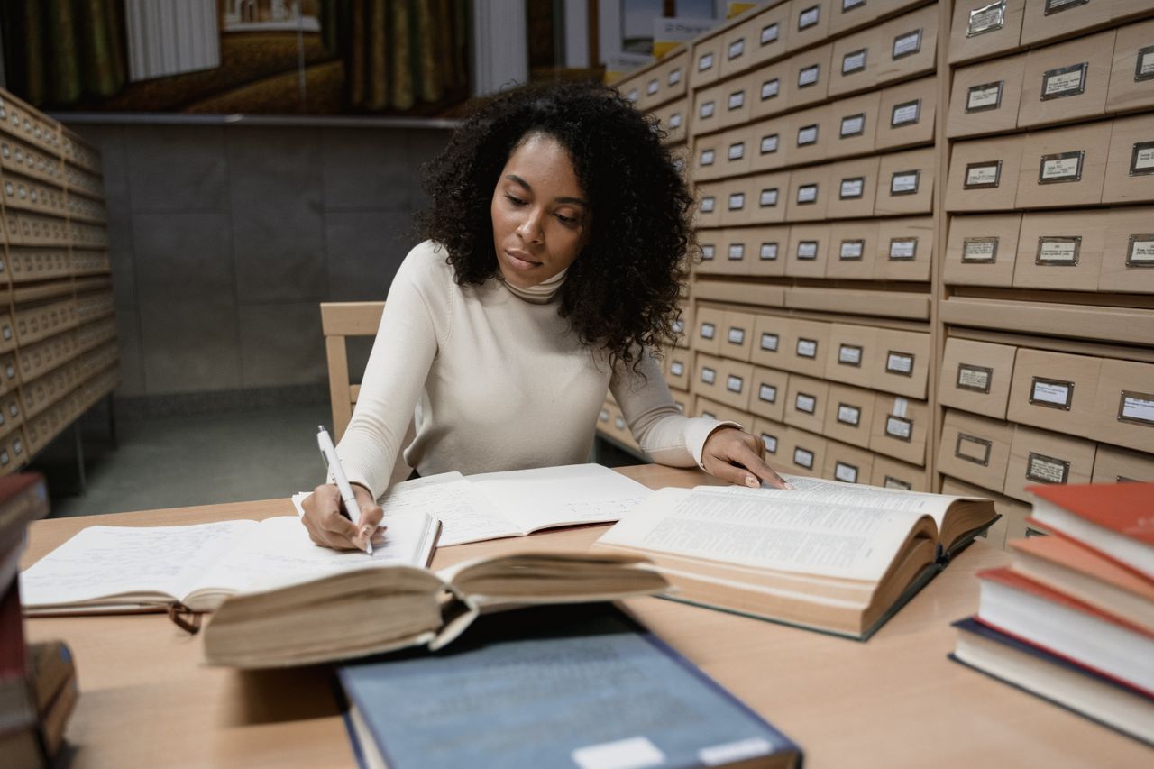 Services Woman taking notes in a library with books and a card catalog for research purposes.